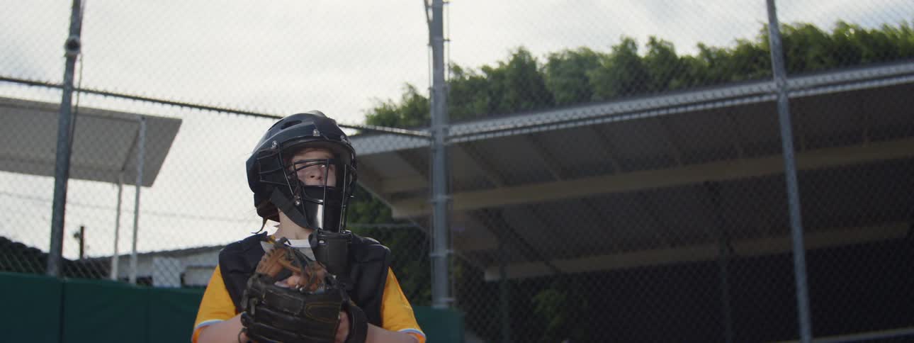 Youth baseball catcher in protective gear makes a slow-motion catch and then throws the ball
