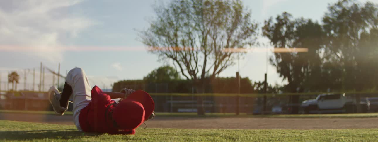 A young baseball player in a red uniform makes a spectacular diving catch and proudly shows off the ball in slow motion