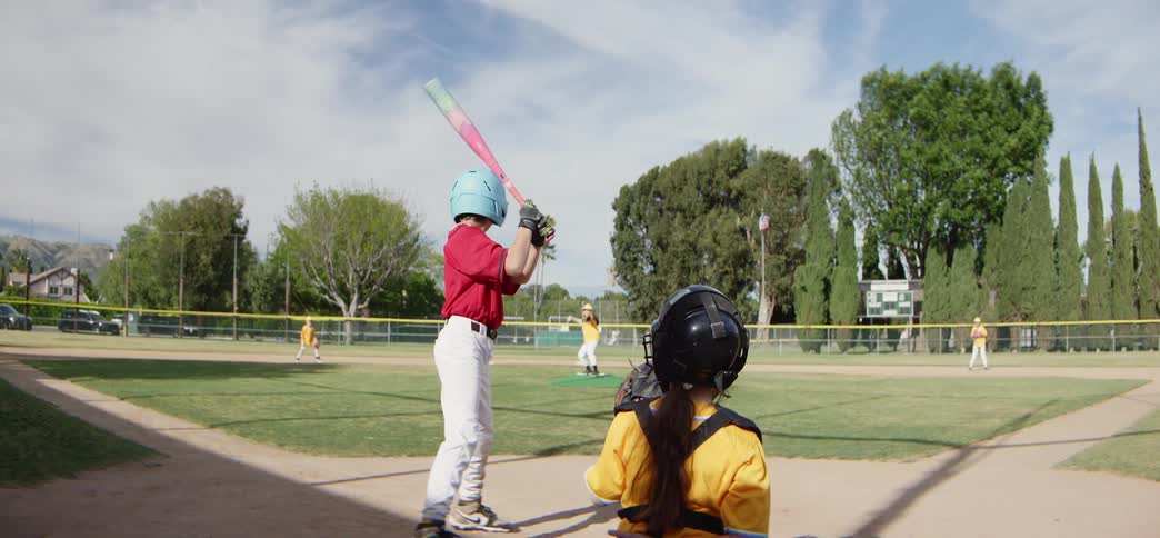 Slow motion over-the-shoulder view of a young batter hitting a baseball during a youth league game