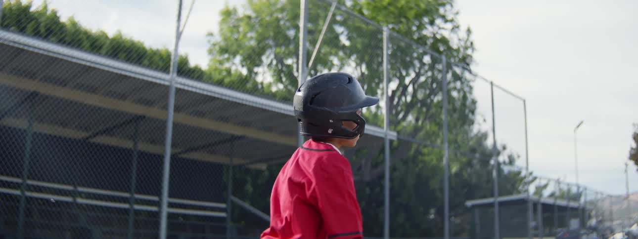 A young boy in a red uniform and batting helmet swings his baseball bat in dramatic slow motion during a game