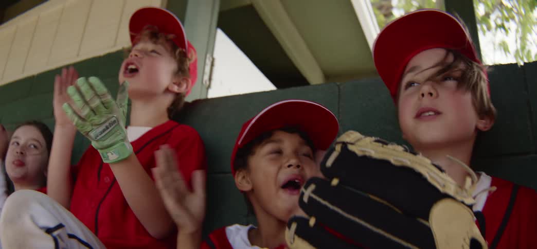 Enthusiastic young baseball players cheer for their team from the dugout bench in slow motion