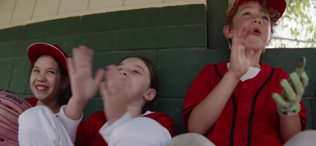 A slow-motion close-up of excited young baseball players in red uniforms cheering and clapping for their teammates from the dugout