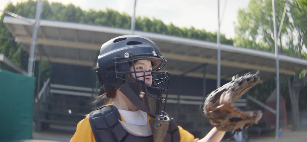 Slow motion close up of a young female baseball catcher in full gear catching and throwing a ball during practice