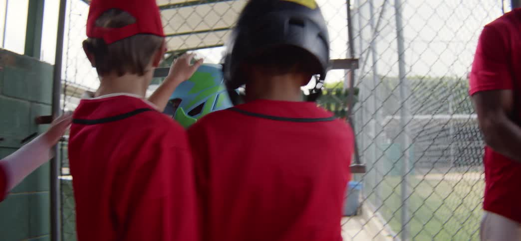 A youth baseball coach helps a young batter with his helmet before he's cheered on by his teammates in the dugout