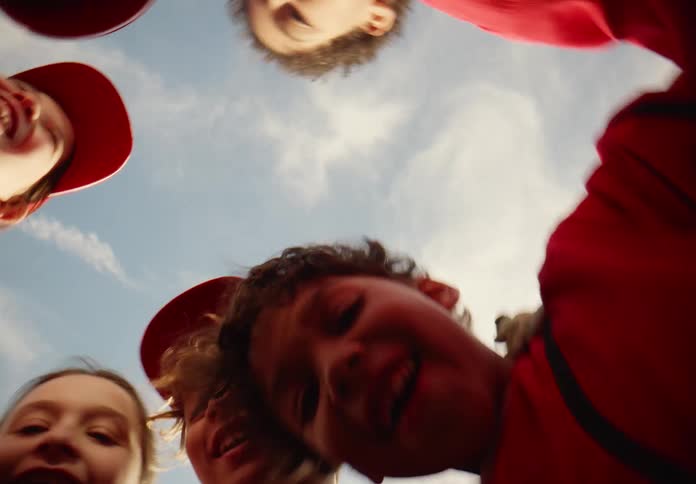 A low-angle view of a diverse group of smiling children in red uniforms huddled together under a blue sky