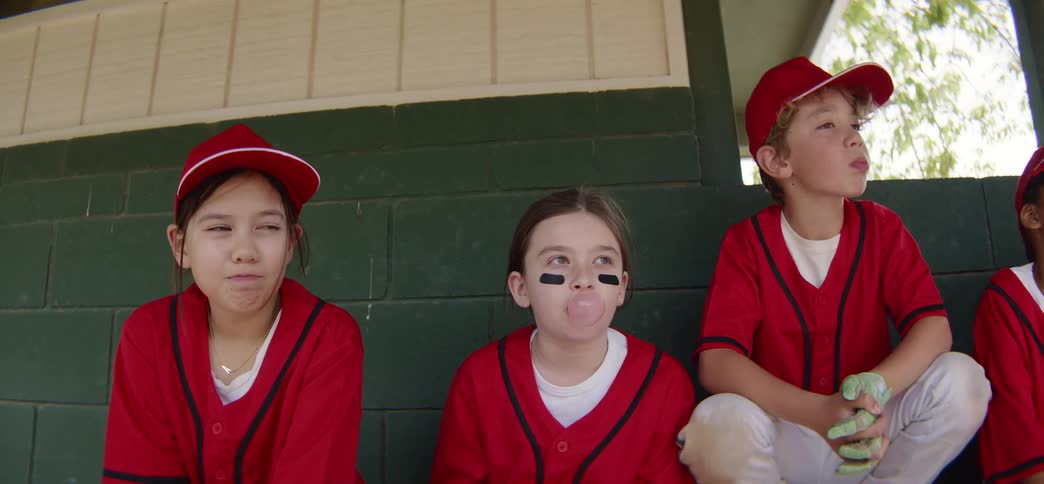 Little league baseball players in red uniforms cheer on their team from the dugout in slow motion