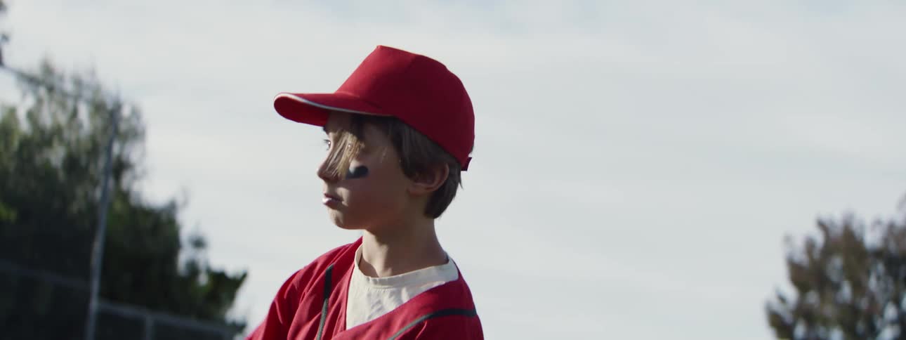 Slow motion shot of a focused young baseball pitcher in a red uniform throwing a ball on a sunny day