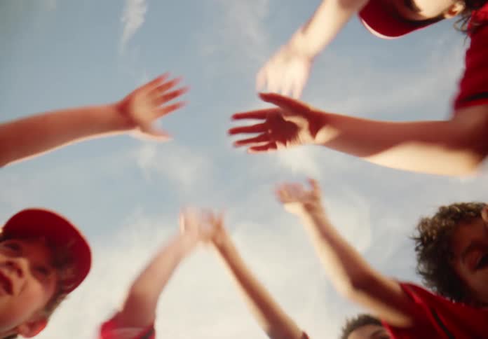 Unified kids' sports team huddles together, stacking their hands before breaking apart in a cheer, shot from below