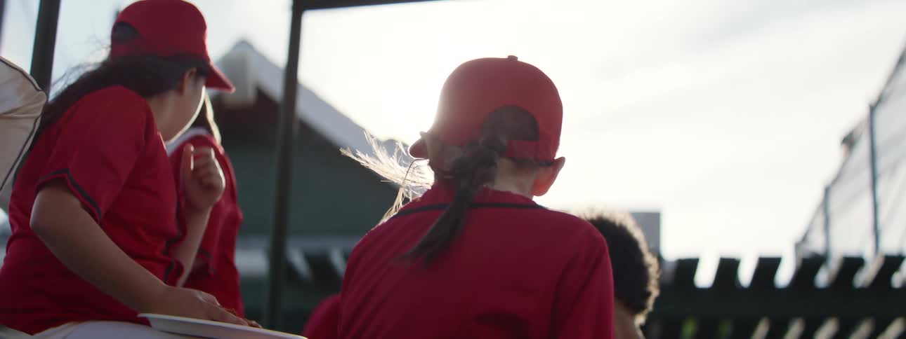 Slow motion shot of a young girl with braided hair listening to her teammates in a sunny dugout