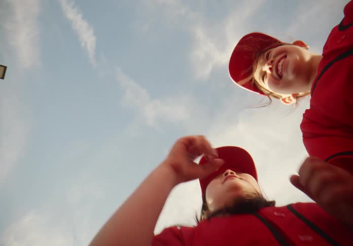 From below, a joyful team of young baseball players in red uniforms gather in a huddle, celebrating together under a sunny sky