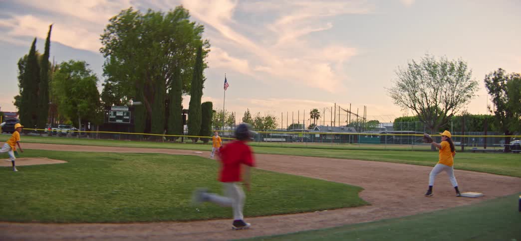 A young baseball player is tagged out at the base in slow motion during a little league game at sunset