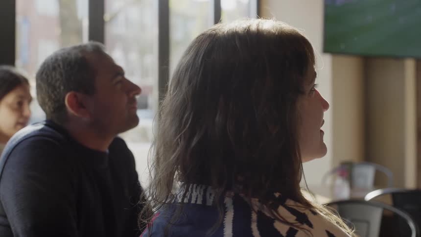 A group of friends gather in a sunlit pub to watch a televised sports game together