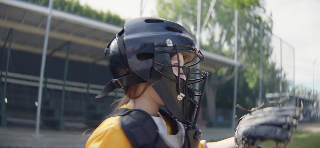 Slow motion side view of a young female baseball catcher in full gear practicing catching and throwing the ball