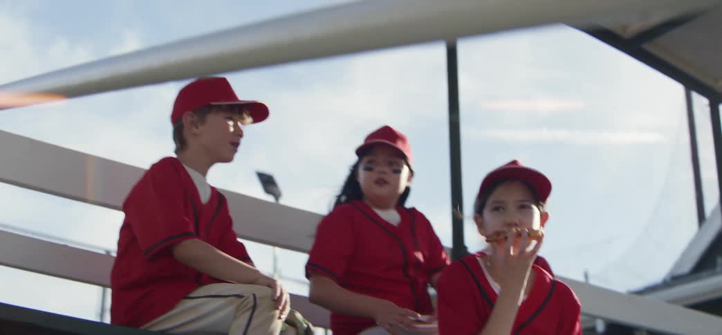 A youth baseball team in red uniforms celebrates with high-fives and cheers from the dugout bench in slow motion