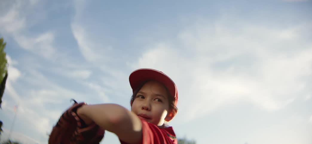 Low angle slow motion shot of a young girl in a red uniform throwing a baseball on a sunny day