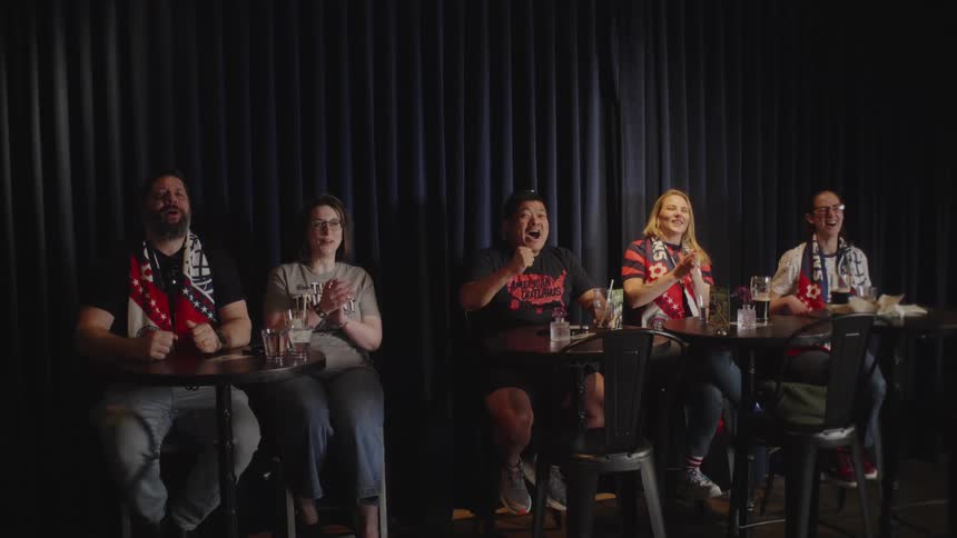 A group of enthusiastic and diverse friends wearing team scarves cheer and celebrate in slow motion while watching a game at a bar