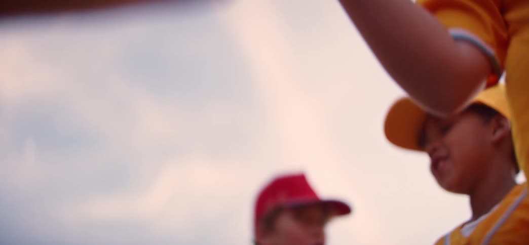 A slow-motion close-up shot captures young baseball teammates high-fiving in a line, showing good sportsmanship after a game