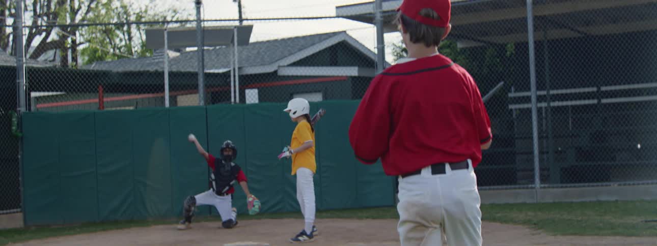 Slow motion over-the-shoulder view of a young boy pitching and then catching a pop fly during a little league baseball game