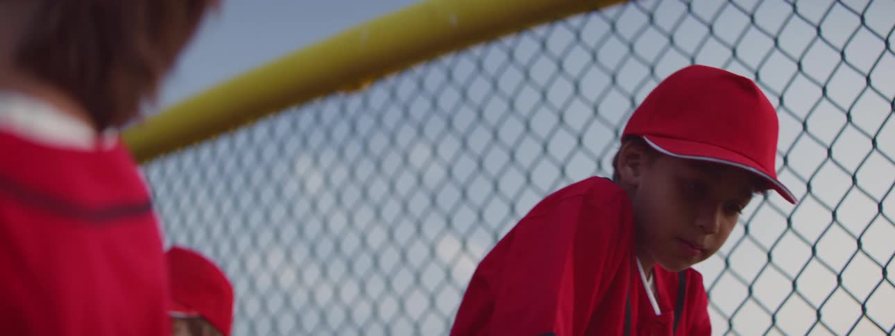 Slow motion close-up of a little league player in a red uniform talking with a friend at the baseball field