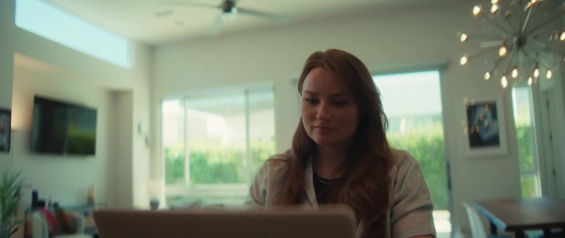 A dolly-in shot of a young professional woman working from home on her laptop in a bright, modern living space