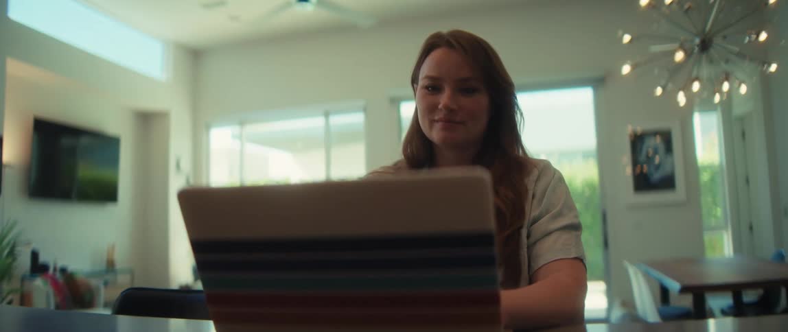 A smiling woman works on her laptop at the kitchen island in a modern home as the camera slowly pushes in