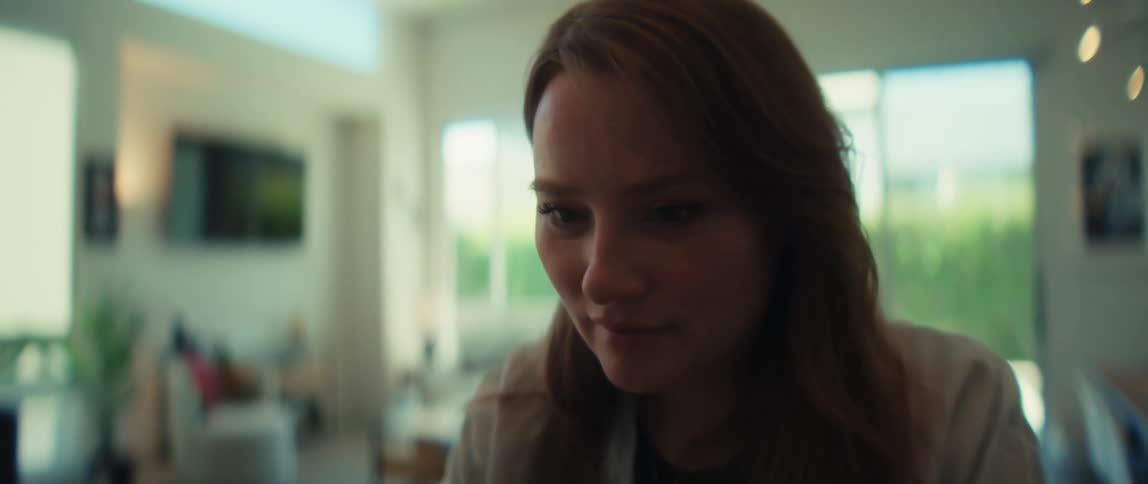 A focused young woman breaks into a gentle smile while working from her modern, sunlit home