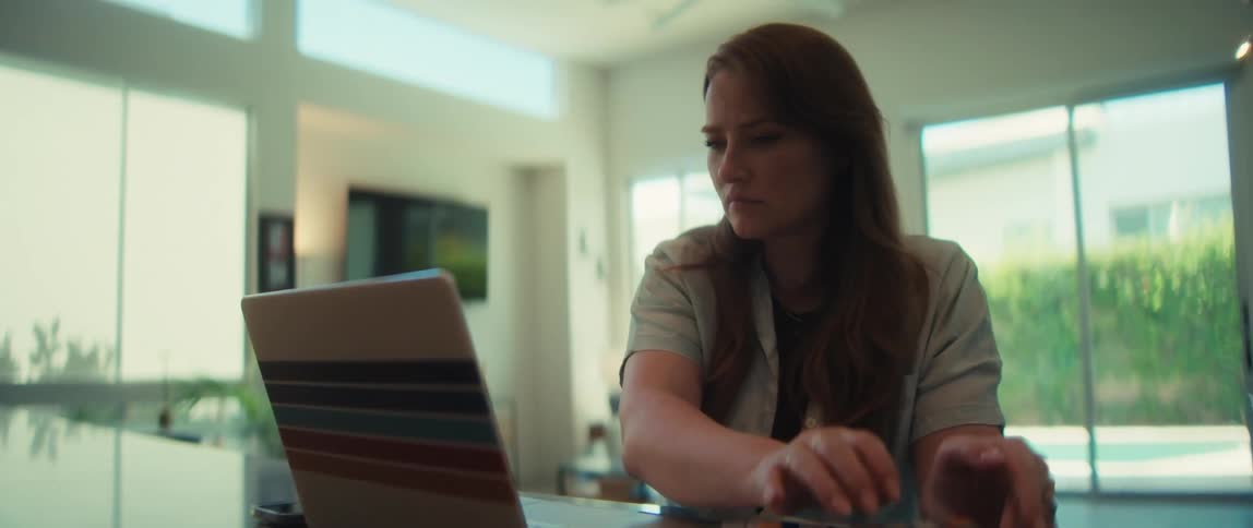 A woman working from home types on her laptop and then uses a calculator, looking focused on her work