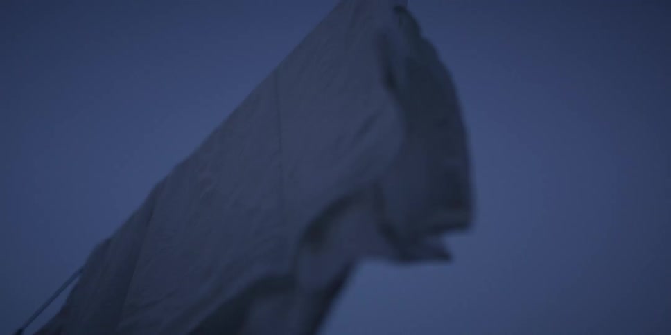 A moody low angle shot of a white sheet on a clothesline blowing gently in the wind at twilight in slow motion