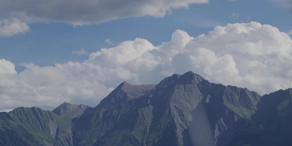 A beautiful timelapse shows clouds rolling over a majestic green and rocky mountain range