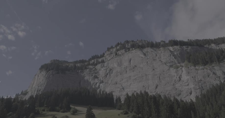 A time-lapse of white clouds moving across a blue sky over a majestic, tree-covered rock cliff