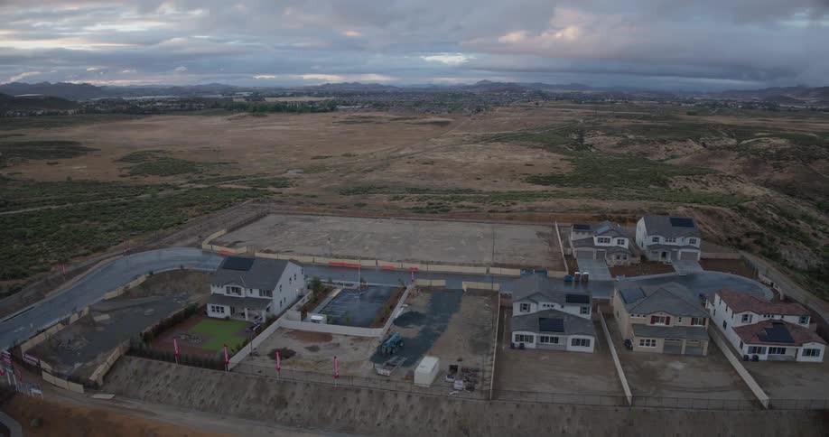 Aerial time-lapse shows the construction and expansion of a new suburban housing development in a rural, hilly landscape at dusk