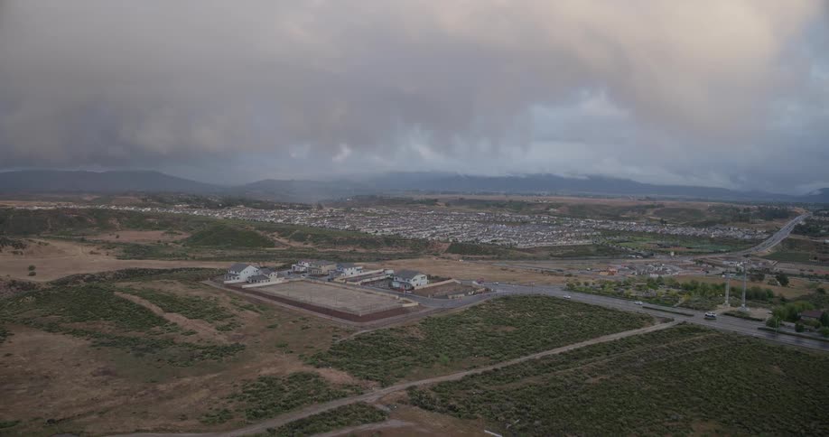 Aerial drone footage slowly pushes toward a new housing development on the edge of a large suburban community under a cloudy sky