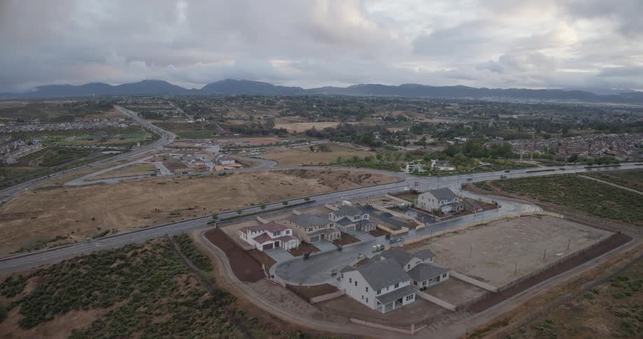 An aerial view reveals a new suburban housing development under construction, expanding into the rural landscape on an overcast day