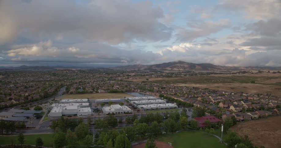 An aerial view of a suburban school and residential community nestled in a valley with mountains in the background on an overcast day