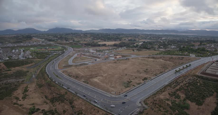 A static aerial view of a curving highway through a developing suburban landscape with distant mountains under an overcast sky