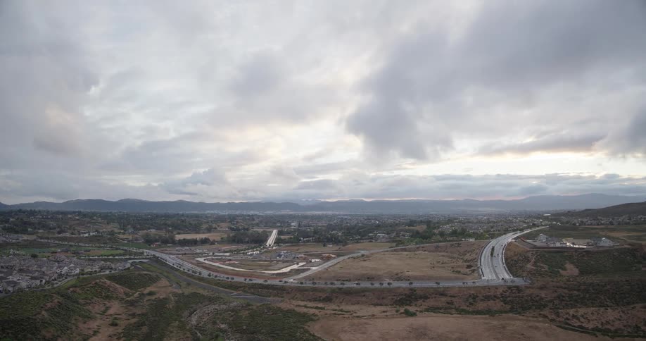 A wide landscape view of a highway winding through the hills of a suburban town under a cloudy sky