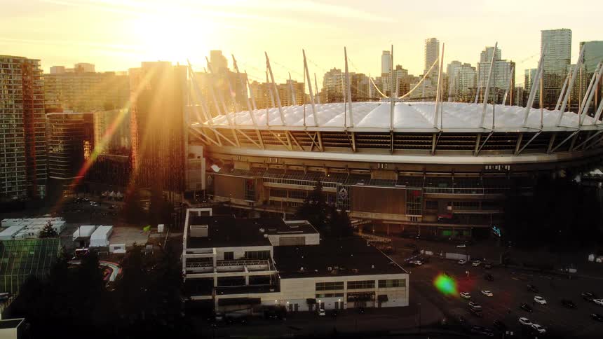 An epic aerial view of Vancouver's BC Place stadium as the golden sun sets behind the city skyline, creating a beautiful lens flare
