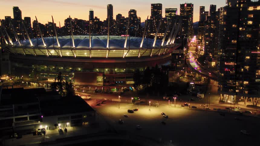 Slow aerial pull-back and tilt-up reveals the illuminated BC Place stadium and the Vancouver skyline at dusk