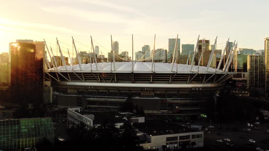 A cinematic aerial shot reveals BC Place stadium in downtown Vancouver as the golden sun sets behind the city skyline