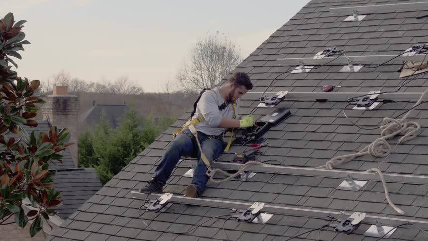 Man wearing safety ropes is working on roof of house