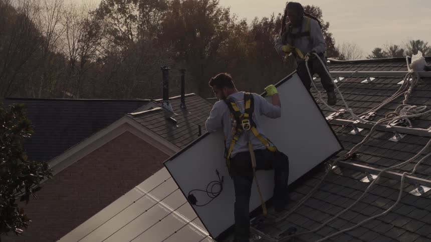 Workers install solar panels on a roof