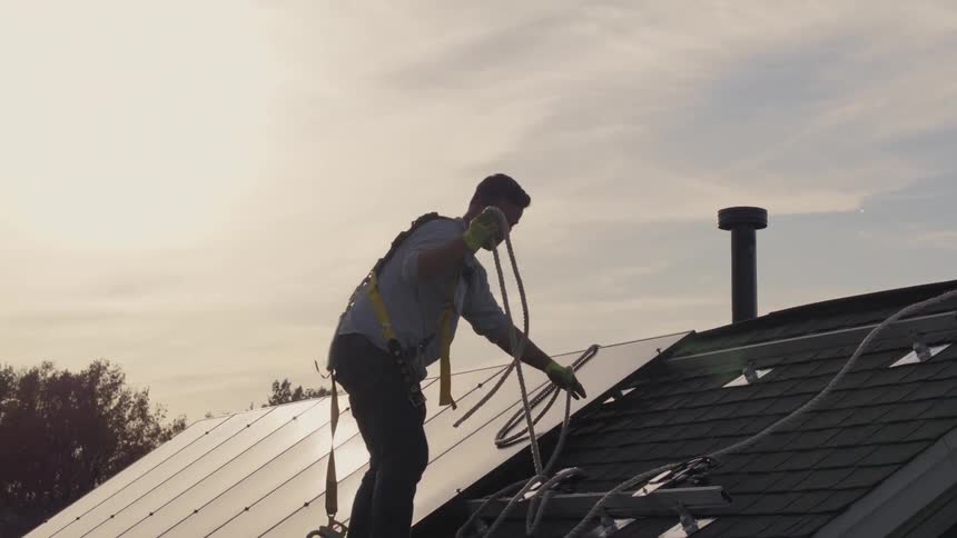 A man on a roof coils rope while installing solar panels