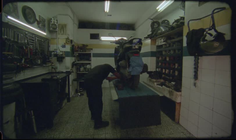 Vintage-style slow zoom shot of a mechanic diligently working on a scooter in a gritty, fluorescent-lit workshop