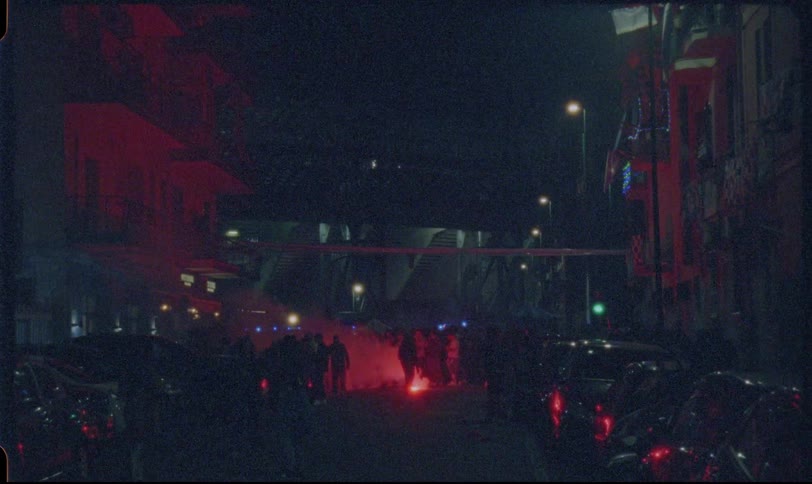 Vintage-style footage of a tense nighttime protest on a city street with red smoke from a flare and flashing police lights
