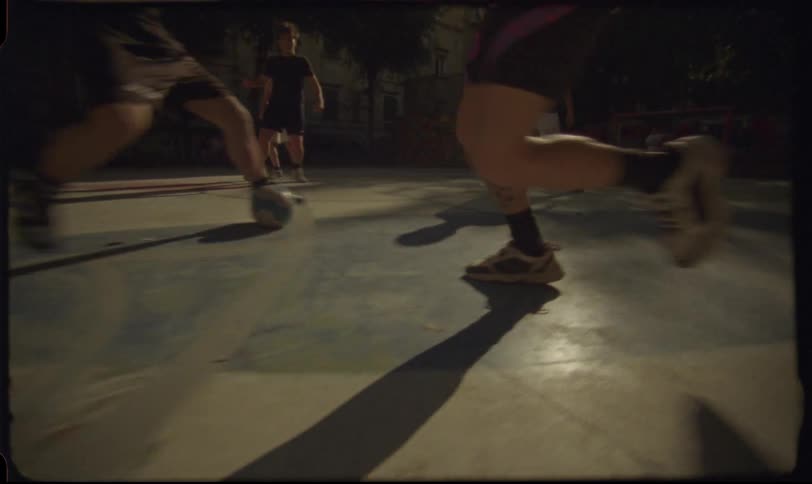 A slow-motion, low-angle vintage shot shows the legs of several men as they play soccer on a court at night