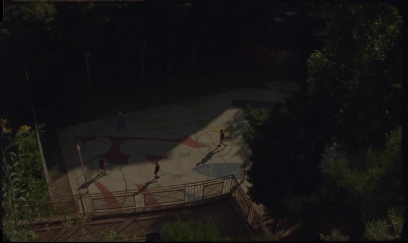 Nostalgic Super 8 footage tilts from a sunny Italian cityscape down to a group of children playing on a colorful sports court
