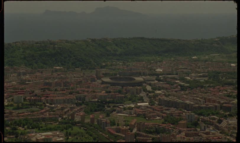 A vintage, film-style aerial shot slowly zooms in on the cityscape of Naples, Italy, revealing the iconic stadium by the sea