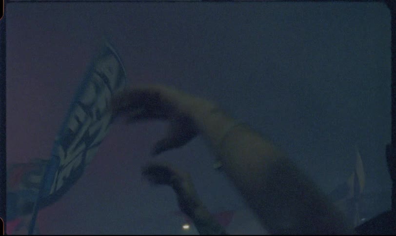 Vintage-style footage of an energetic crowd waving flags and filming on their phones at a nighttime event