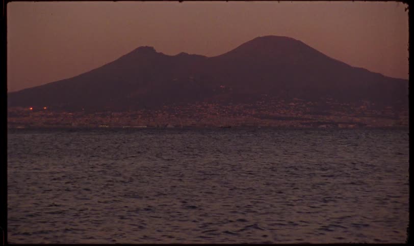 Vintage footage shows the silhouette of Mount Vesuvius across the calm sea at dusk