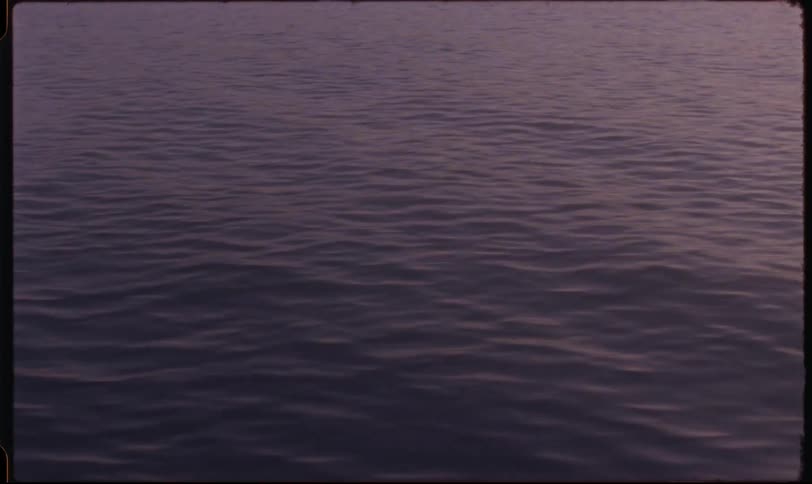A close-up shot of calm water with gentle ripples reflecting the purple twilight on vintage film